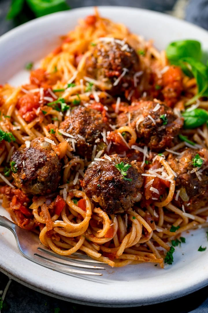 Meatballs and spaghetti on a white plate with basil and parsley