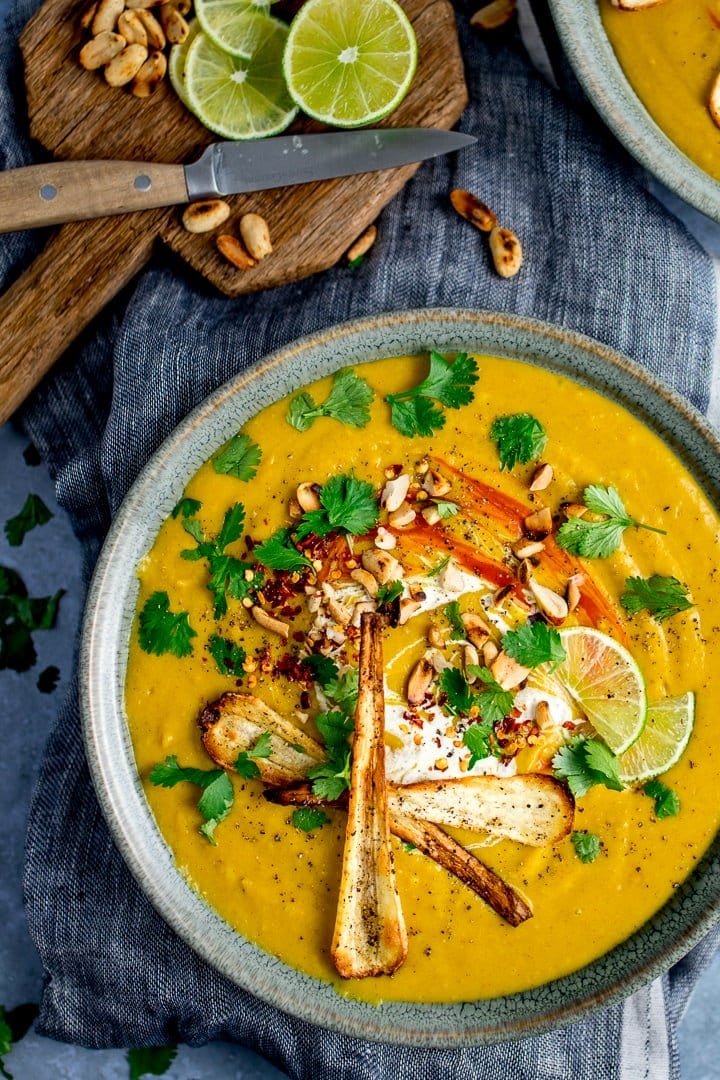 Tall image of parsnip and sweet potato soup on blue background. Toppings scattered around an on soup.