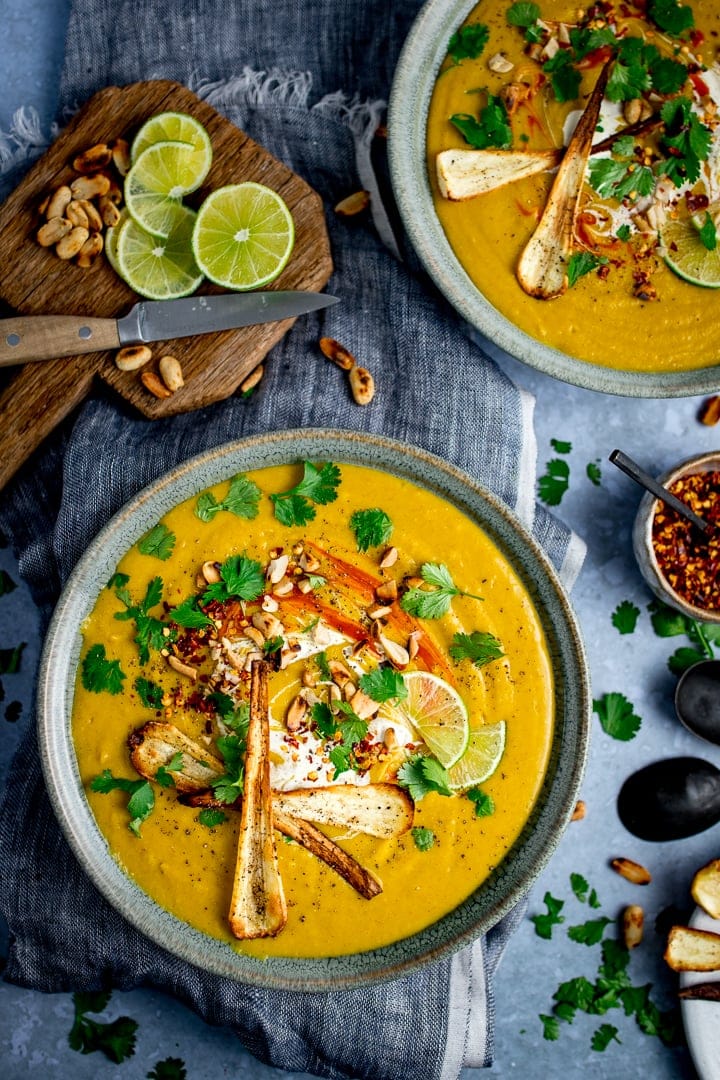 overhead picture of Spicy Parsnip and Sweet Potato Soup in a dutch oven with some having been ladled out into a white bowl on a blue and white chequered table cloth