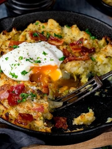 bubble and squeak in a pan with a portion taken out. Running poached egg on top