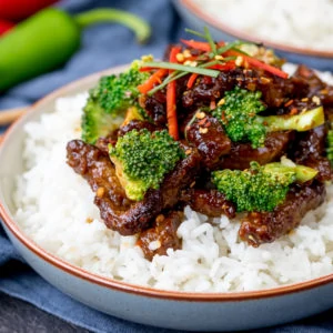 Bowl of rice topped with crispy beef strips in a tangy spicy sauce with broccoli.