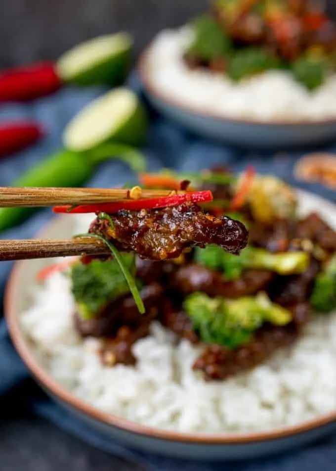 Chopsticks taking a piece of beef from a bowl of crispy beef and broccoli with rice