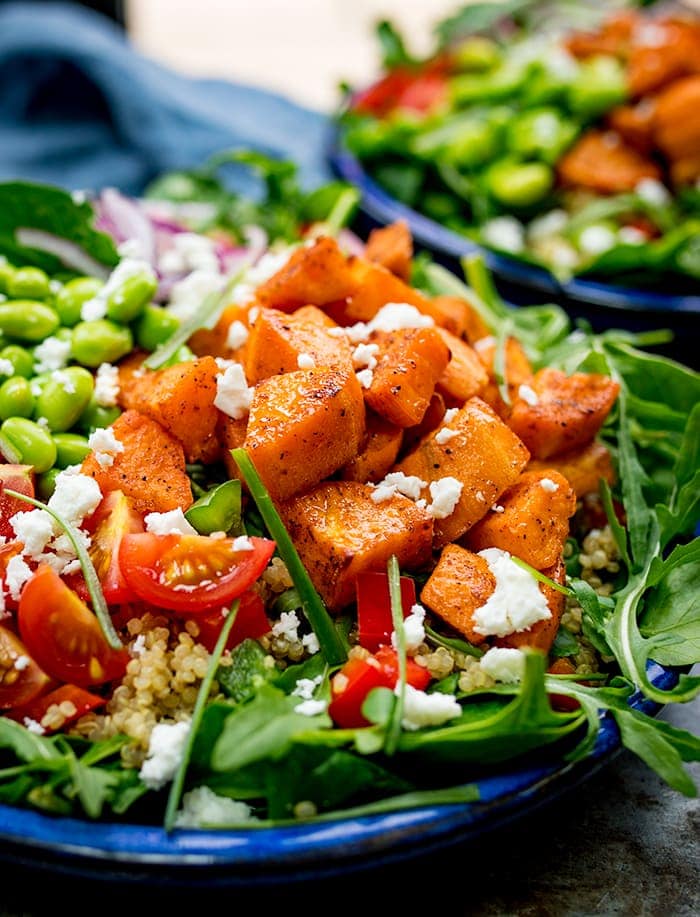 Close up of a bowl of salad with roasted sweet potato, edamame, tomato, quinoa and feta