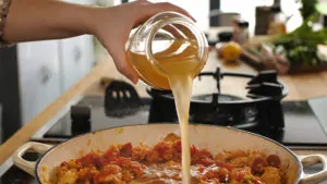 Pouring stock into a pan of jambalaya