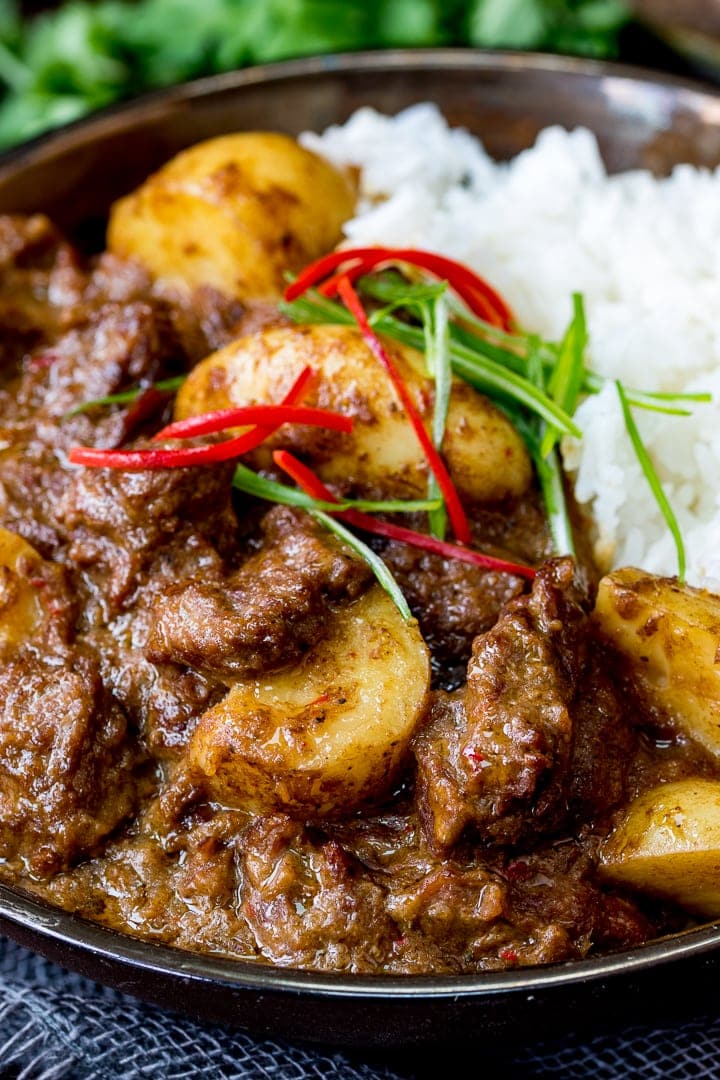 Close up photo of Slow Cooked Beef Massaman Curry in a bowl served with Rice topped with thin strips of chilli