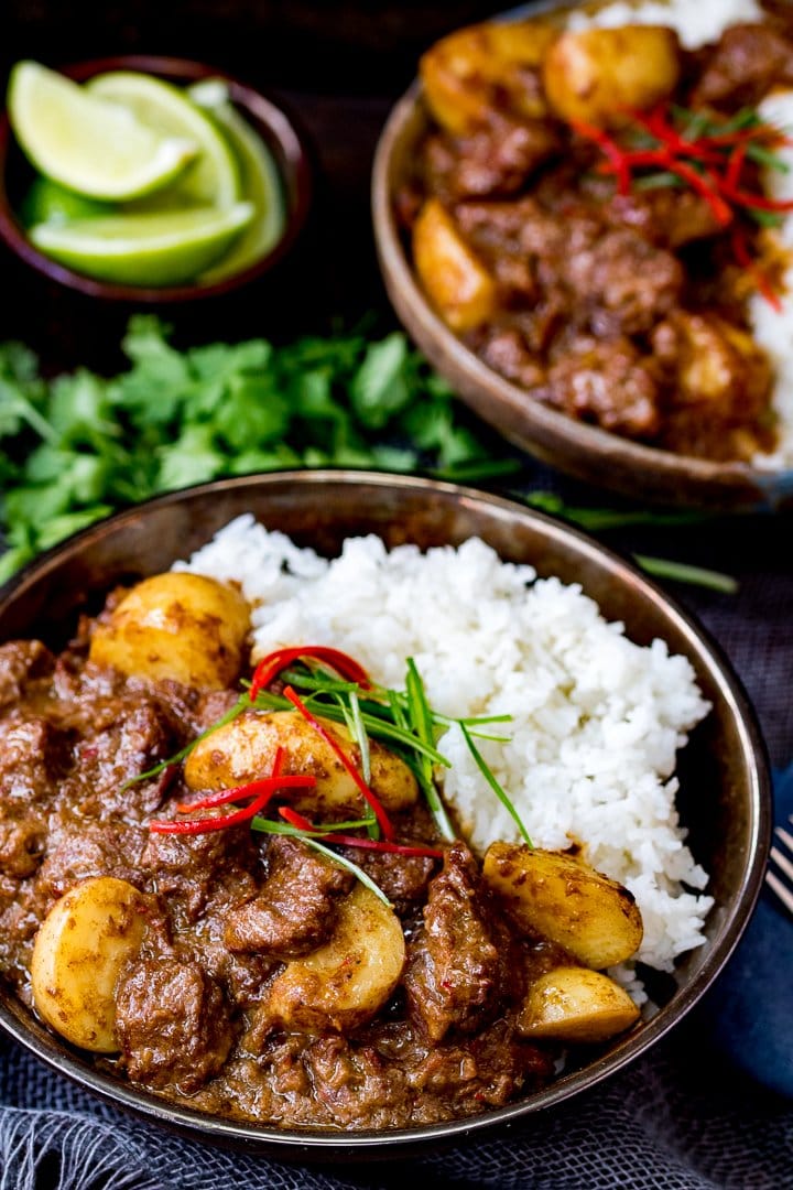 Overhead photo of Slow Cooked Beef Massaman Curry in a bowl served with Rice topped with thin strips of chilli and spring onion. Fresh coriander in the background.