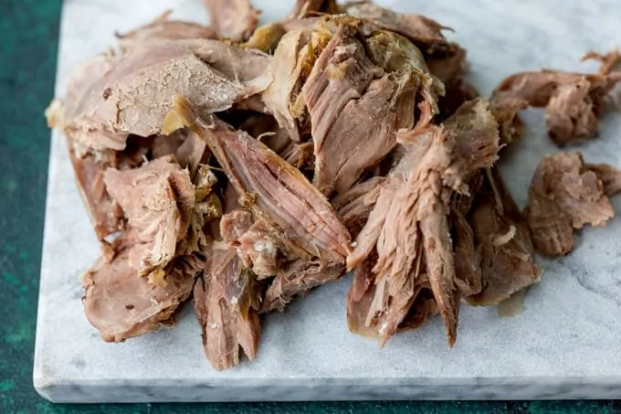 Shredded pieces of leftover roast lamb on a marble board