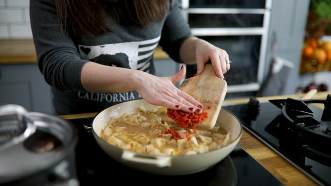 Chopped red chillies being added to a pan of peanut butter chicken curry.