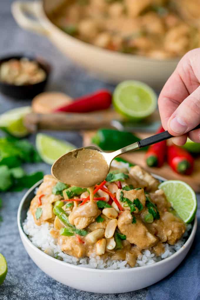 Bowl of rice topped with peanut butter chicken with green beans, chillies and coriander (cilantro). Extra sauce being spooned on top.