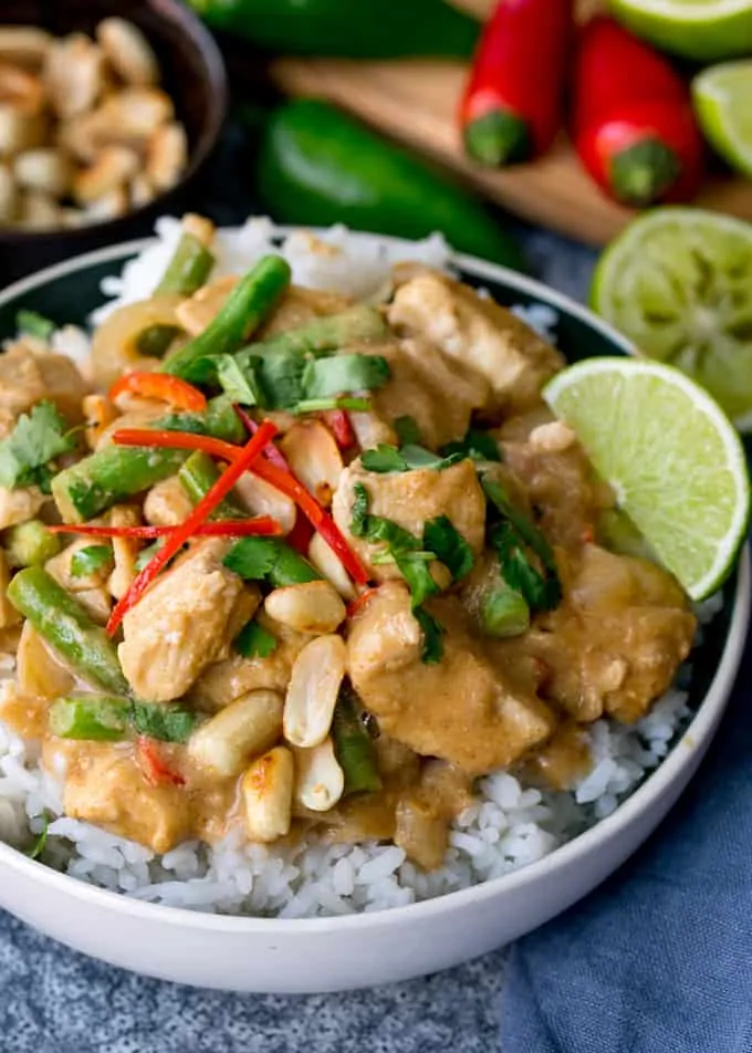 Close up of a bowl of rice topped with peanut butter chicken with green beans, chillies and coriander (cilantro)