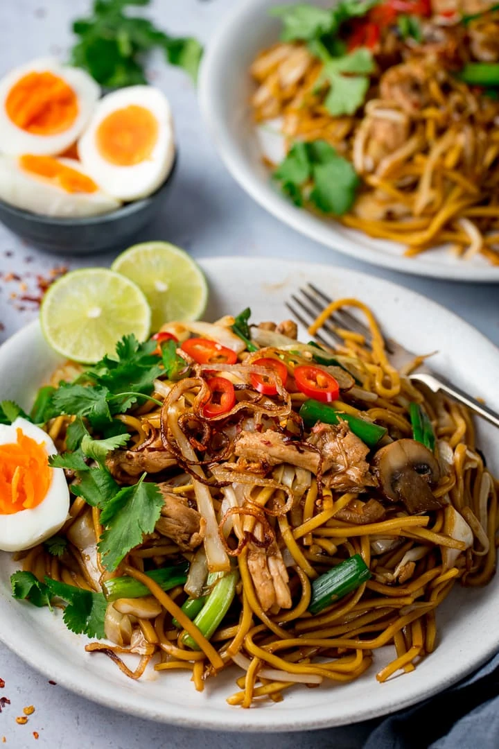 Mee Goreng (asian noodles) on a white plate with hard boiled egg, crispy onions and sliced red chillies