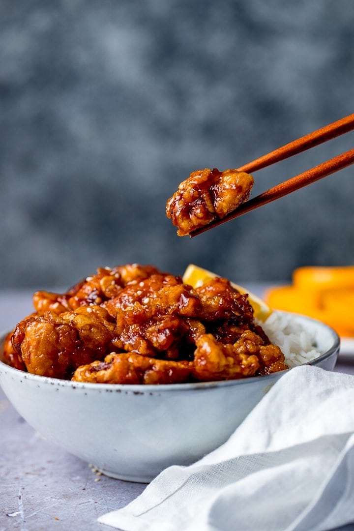 Copycat Panda Express Orange chicken on a blue background being lifted from a bowl with chopsticks