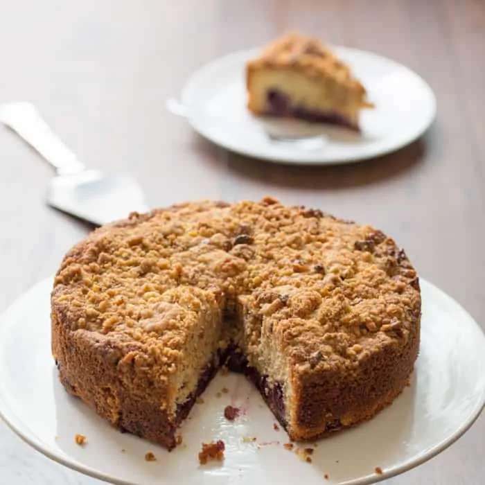 Cherry Crumble Cake on a cake stand with a slice taken out, the slice is in the background out of focus