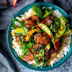 Bowl of sticky chicken stir fry on boiled white rice in green bowl.