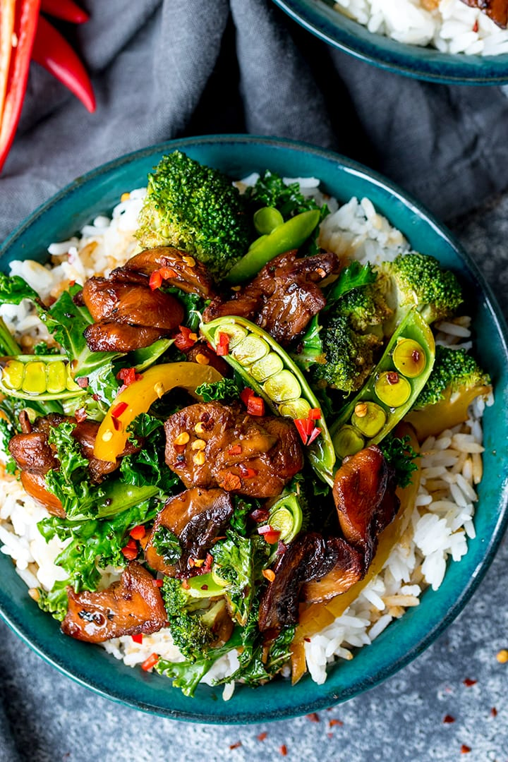 Chicken stir fry with vegetables on rice in a green bowl