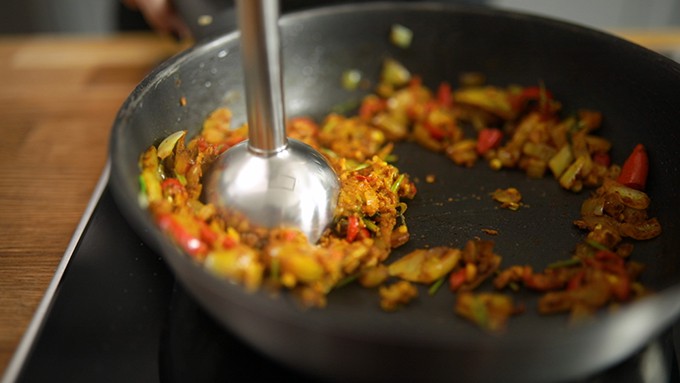 Close up of curry paste ingredients being blended in a frying pan using a stick blender.