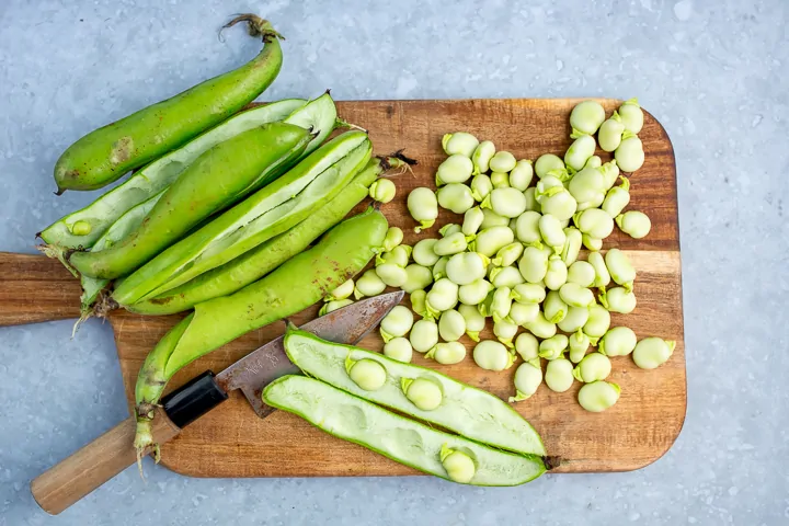 Broadbeans sliced open and removed from pods on a board