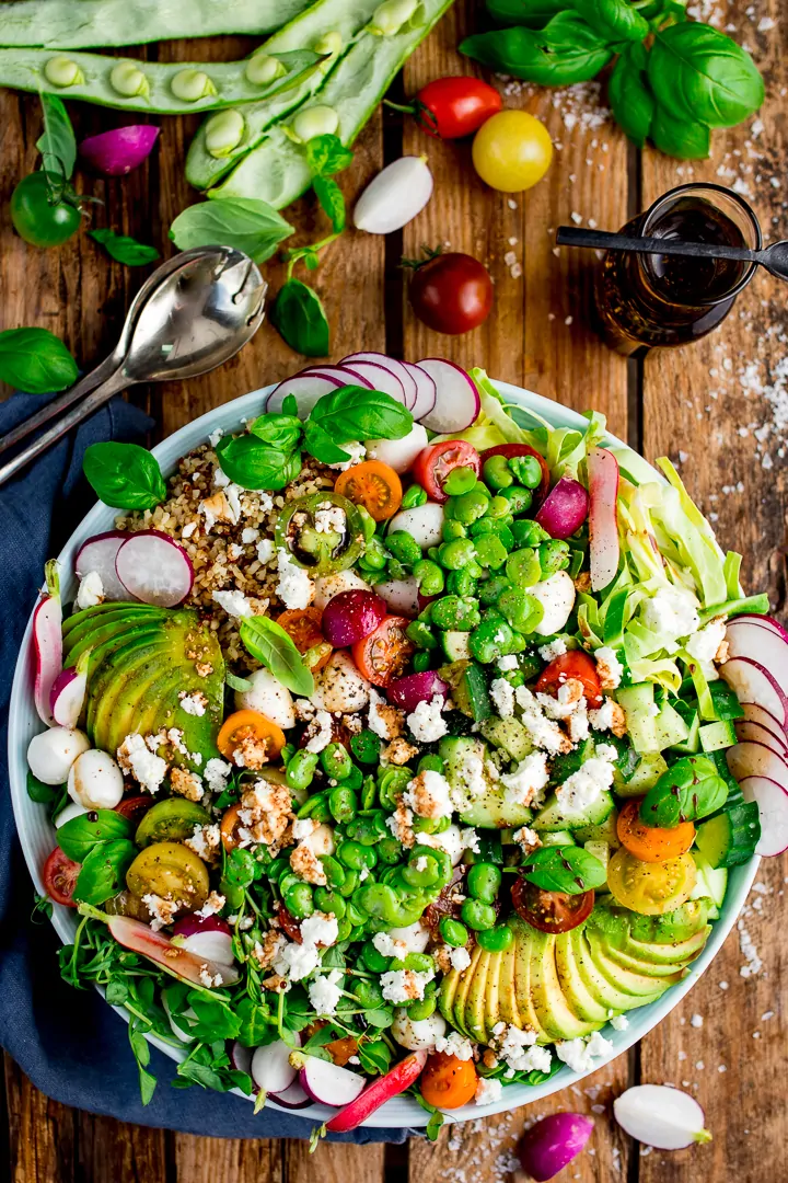 broadbean and quinoa caprese salad on a wooden board with ingredients scattered around