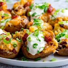 Bacon and cheese potato skins on a plate with sour cream and spring onions