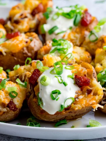 Bacon and cheese potato skins on a plate with sour cream and spring onions