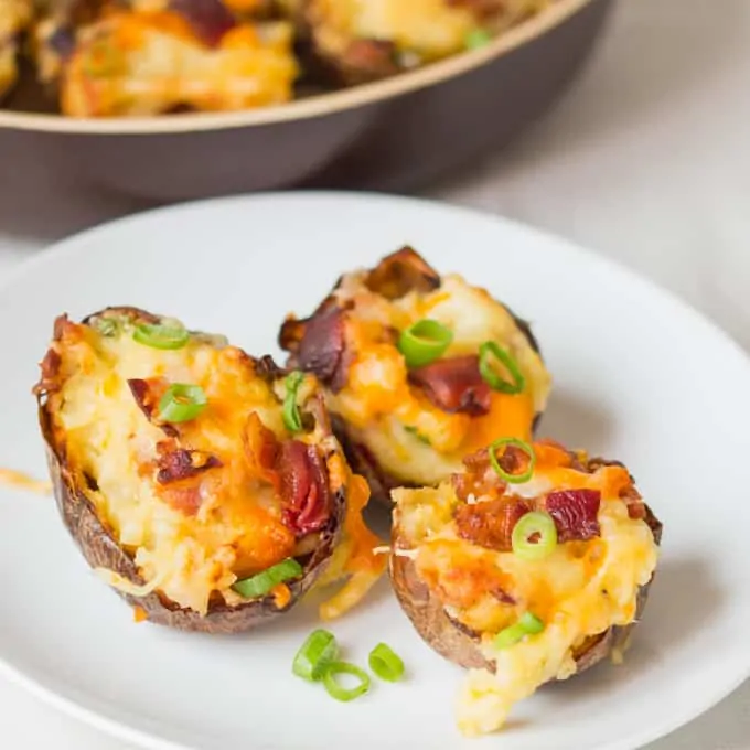 Bacon and cheese potato skins on a plate with sour cream and spring onions