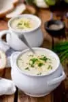 White bowl on a wooden background with cauliflower soup inside. Further bowl in the background.