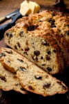 Sliced fruit soda bread on a wooden board with blocks of butter in the background.