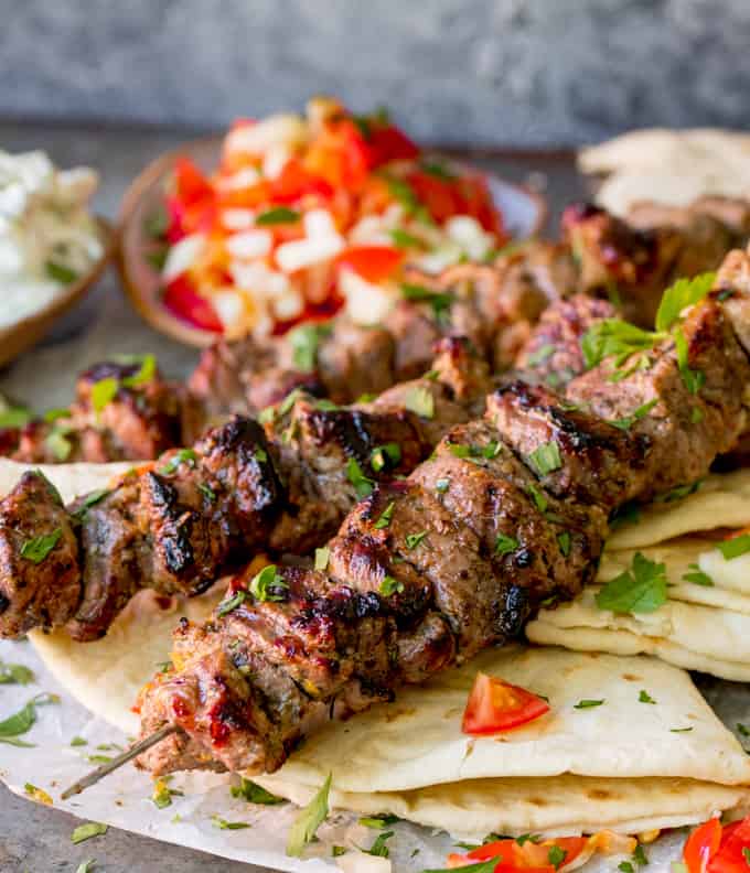 Lamb souvlaki kebabs on top of toasted breads with tomato and onion salad in background