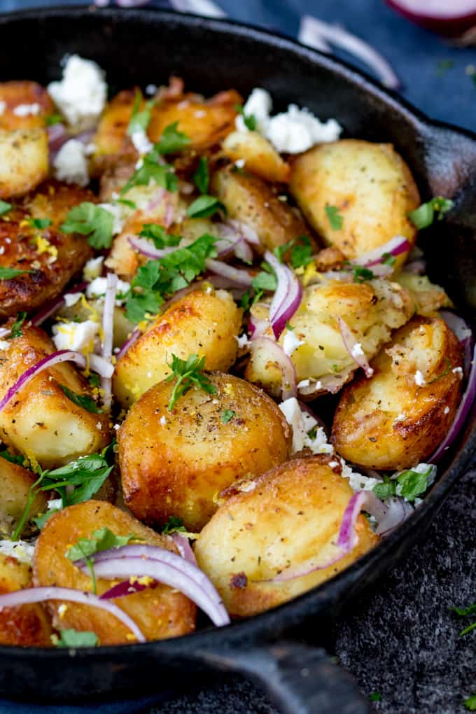 Close up shot of fried Greek potatoes with feta, red onion and parsley in a pan.