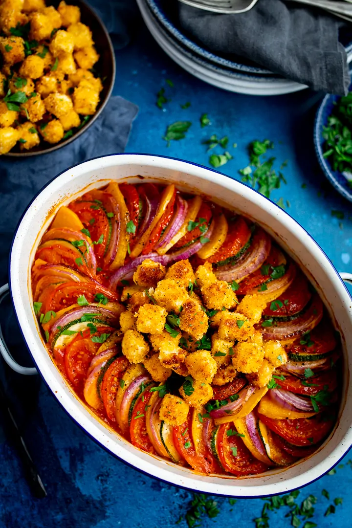 Overhead image of ratatouille in a white dish on blue background