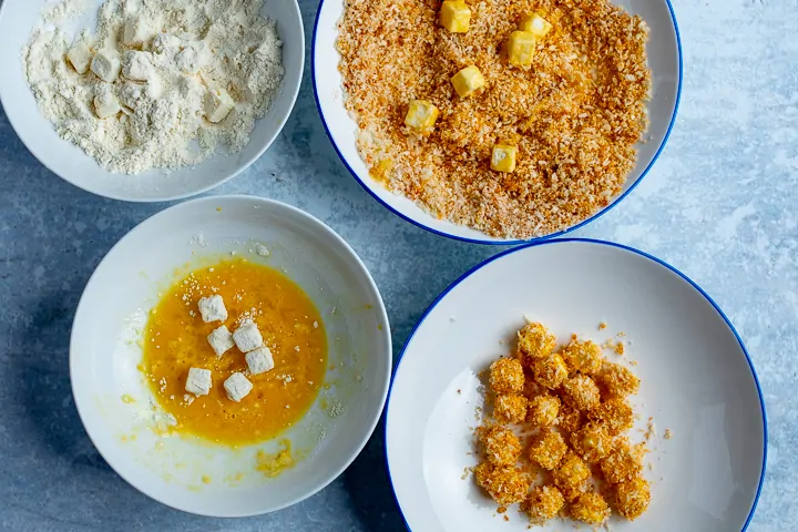 Cubes of feta being floured, dipped in egg and breadcrumbs