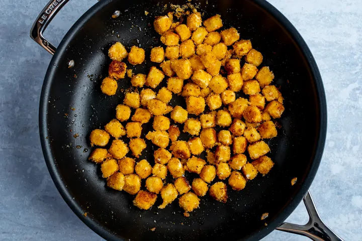 Coated feta cubes being fried in a pan