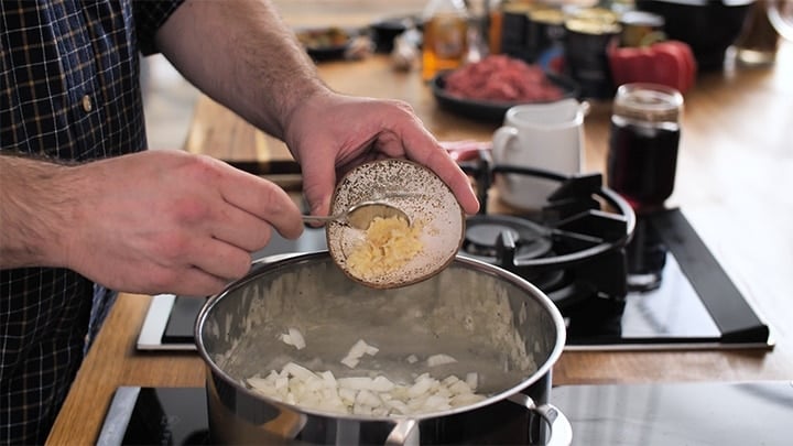 Garlic being added to a pan with onions