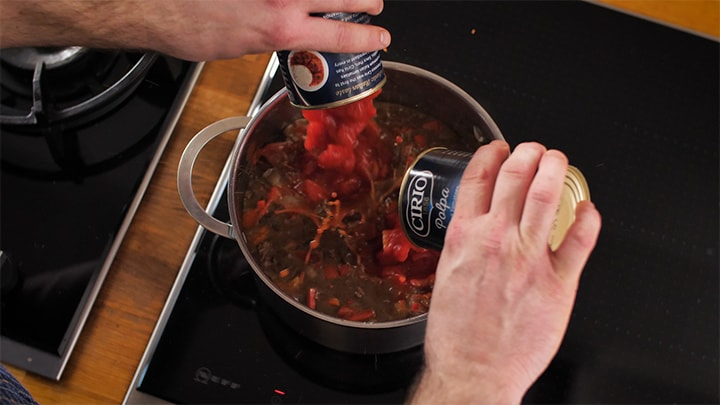 Tinned tomatoes being added to a pan of chilli con carne