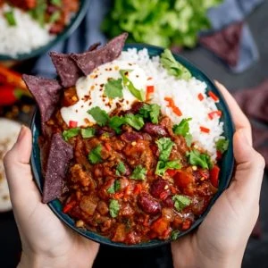 Hands holding bowl of Bowl of chilli con carne with rice
