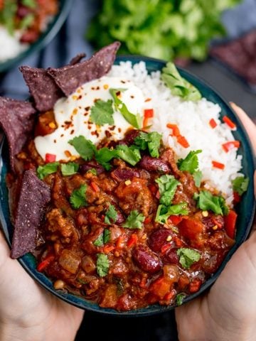Hands holding bowl of Bowl of chilli con carne with rice