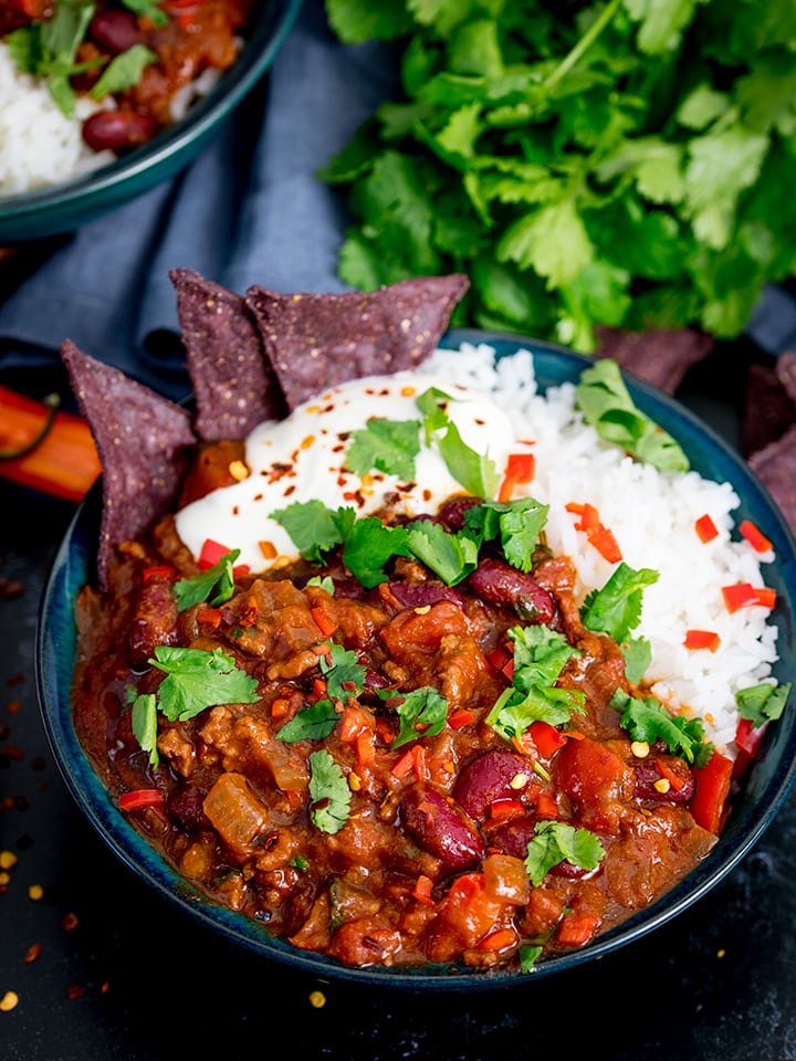 Bowl of chilli con carne with rice and blue corn chips, sprinkled with coriander (cilantro)