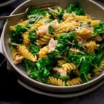 Close up of a bowl of garlic chicken pasta and kale with a fork in the bowl.