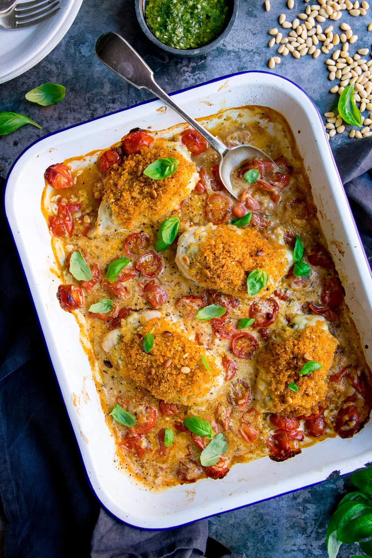 baked pesto chicken in a white tray on a blue background. Spoon sticking out of the dish.