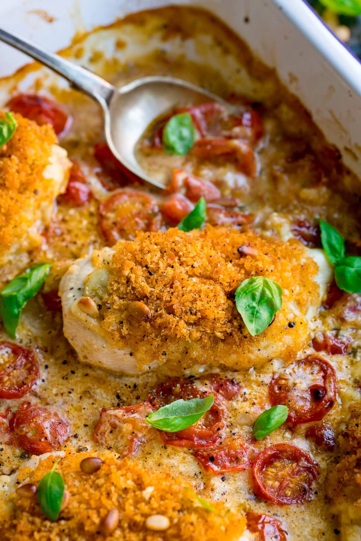 Close up of baked pesto chicken in a dish with a spoonful being taken in the background.