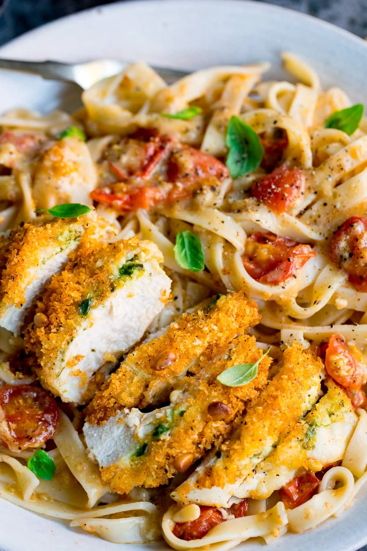 Close up of baked pesto chicken on a plate, sliced into strip and served with tagliatelle.