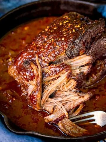 Square image of pulled beef brisket being shredded with a fork