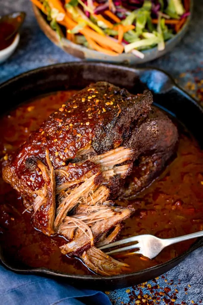 Overhead shot of pulled beef brisket in a spicy tomato sauce in black skillet. Fork is pulling beef apart.