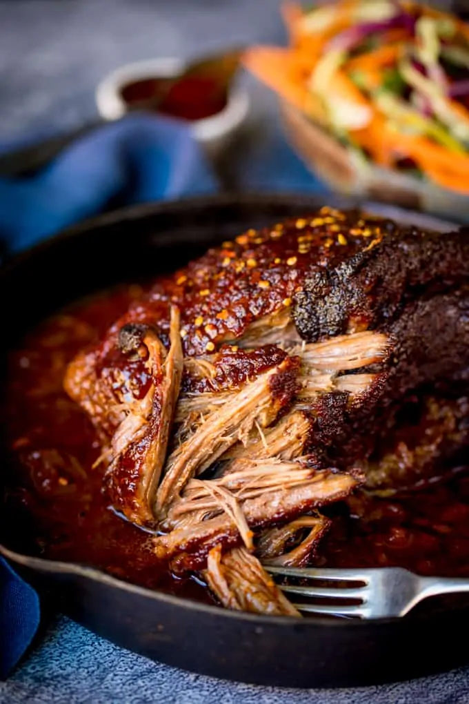 Close up shot of a fork shredding a slow cooked brisket in a black skillet.