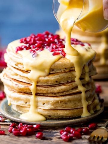 Lemon sauce being poured onto stack of pancakes