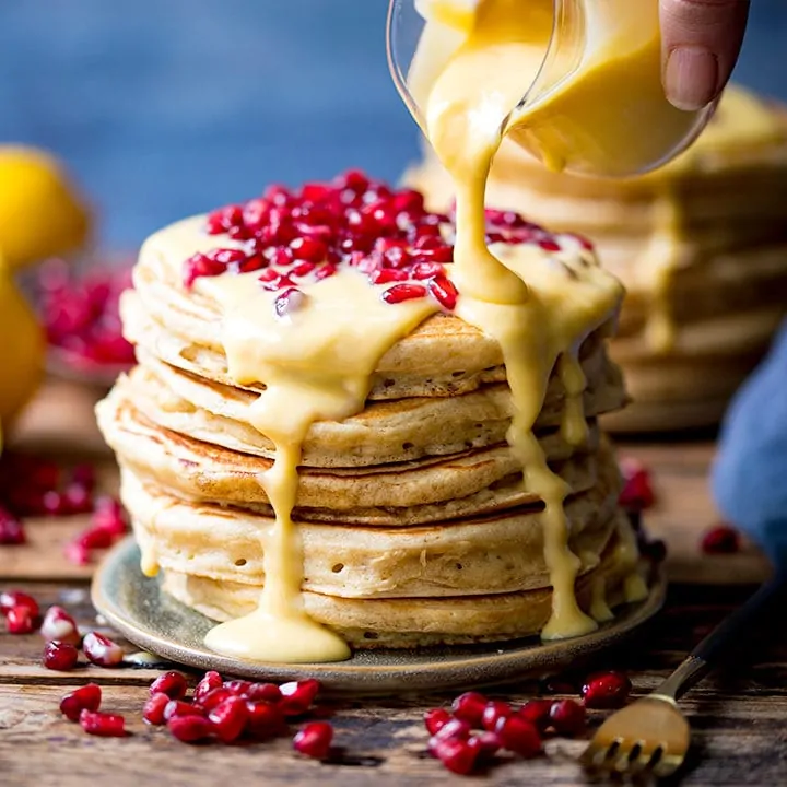 Lemon sauce being poured onto stack of pancakes