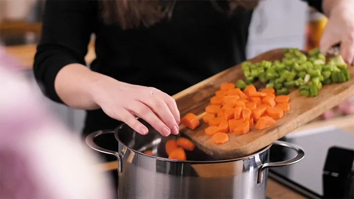 Adding vegetables to a pan for pot pie soup.