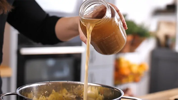 Pouring stock into a pan of chicken and vegetables for pot pie soup