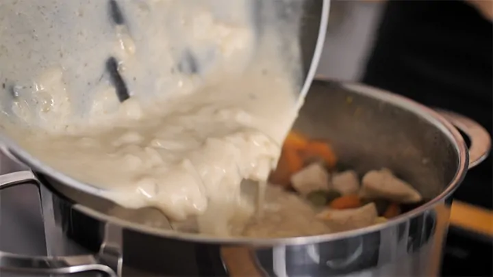 Pouring creamy sauce back into pan with veggies and chicken for pot pie soup