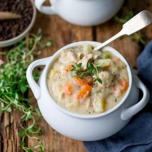 Chicken pot pie soup in a white bowl with fresh thyme on top.